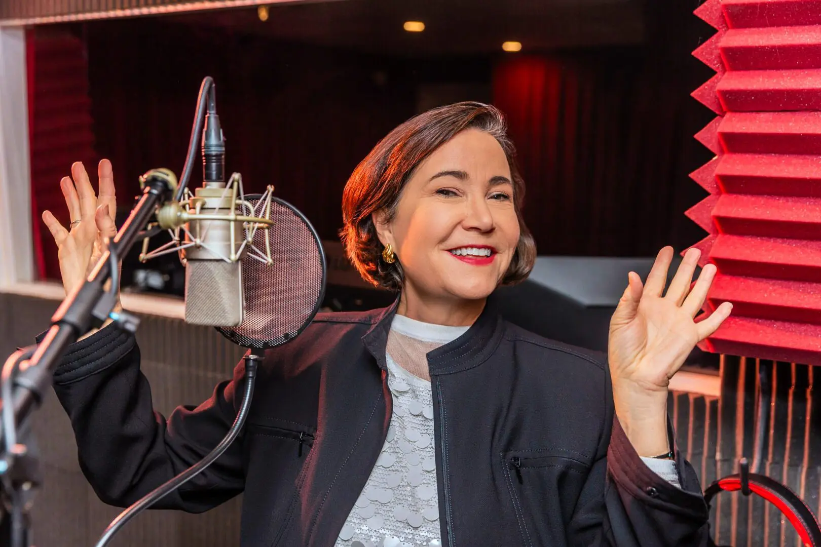 Smiling woman speaking into a microphone in a recording studio.